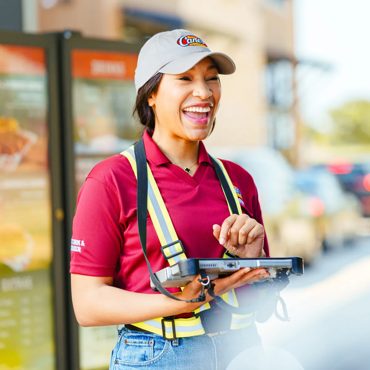 A female employee at Raising Cane's holding a tablet and laughing