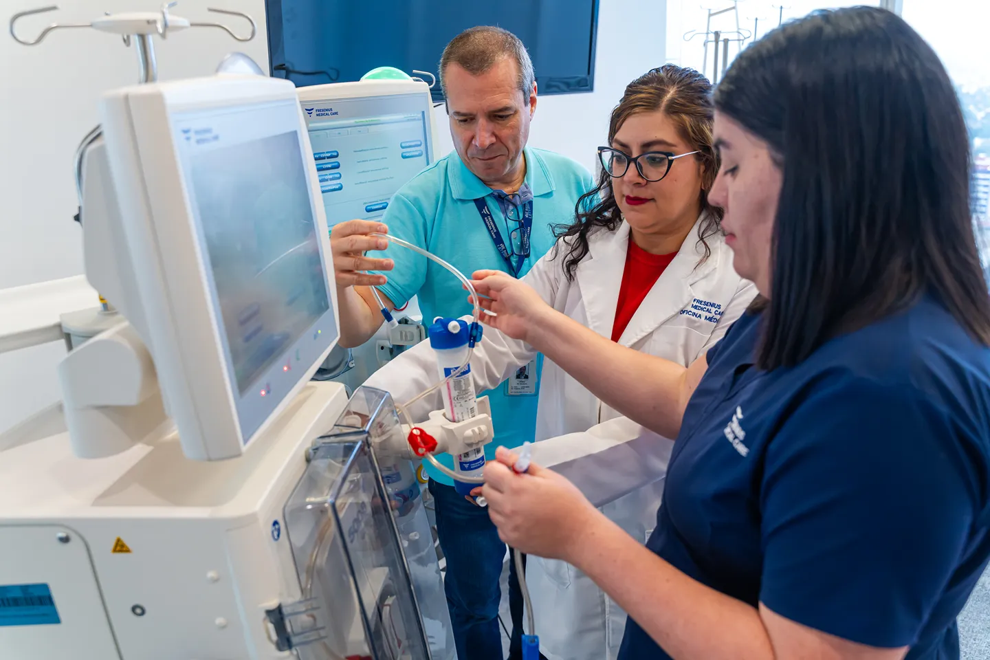 A healthcare worker in protective clothing holds hands and smiles at an older patient receiving medical treatment, while another patient sits nearby in a clinic setting.