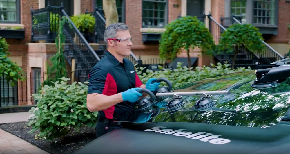 A male Safelite technician in safety glasses and blue gloves using a diagnostic tool inside a car.